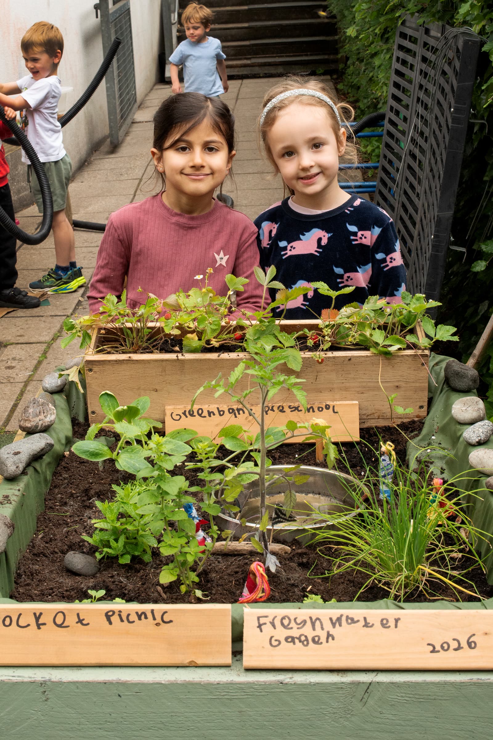 Two children beside the Greenbank Preschool sign in the Pocket Picnic Garden