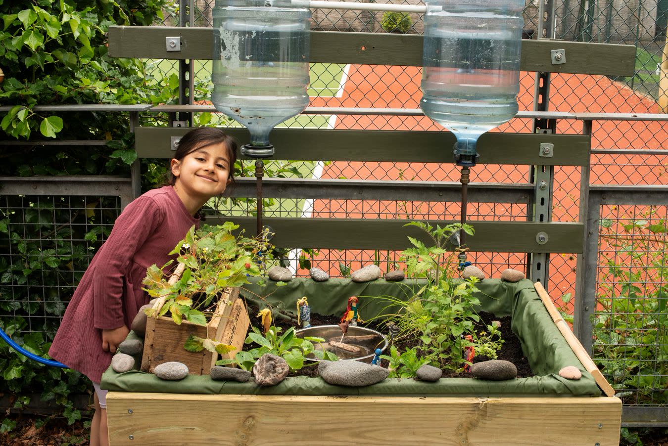 A Greenbank Preschool child beside the Pocket Picnic Garden, with upcycled water collectors and strawberry plants